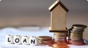 coins, wooden house and block letters arranged to spell LOAN